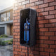 Blue portable charger inside a wall box on a brick facade during rainfall